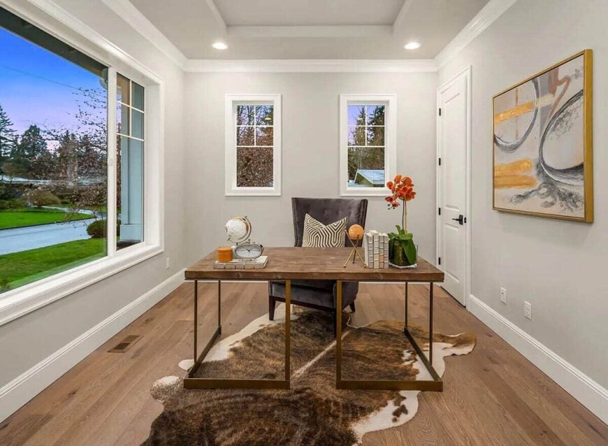 The study has a wood-top desk and a tufted wingback chair sitting on a cowhide rug.