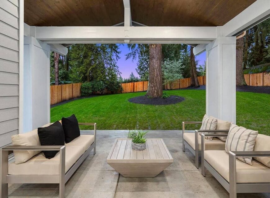 The covered porch is filled with cushioned seats and a wood plank coffee table.