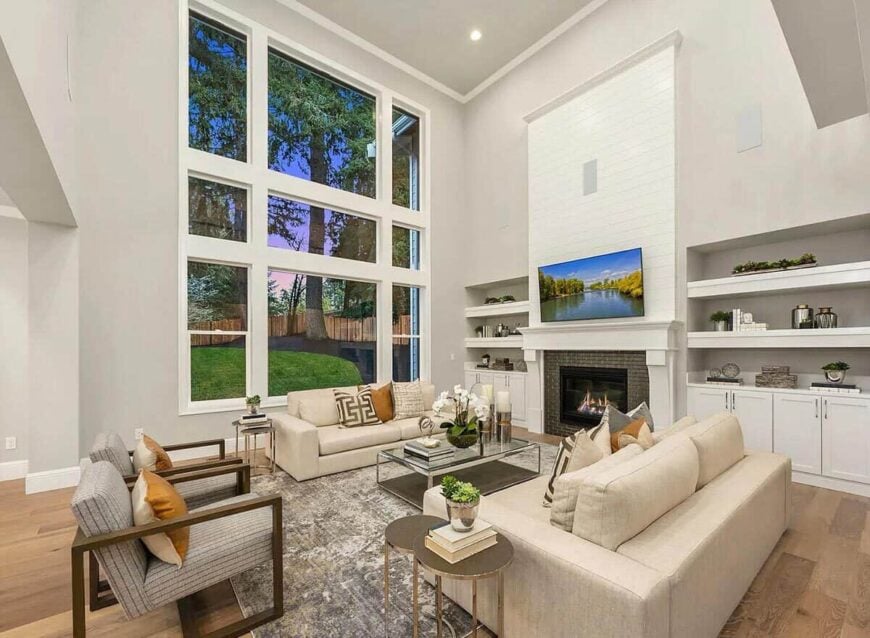 Great room with beige sectionals, a glass-top coffee table, and a fireplace topped with a TV.