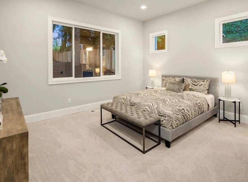 Guest bedroom with carpeted floor and a gray platform bed complemented with a tufted bench.