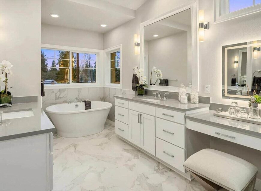 Primary bathroom with a freestanding tub and separate his and her sink vanities where one is attached with a makeup counter.