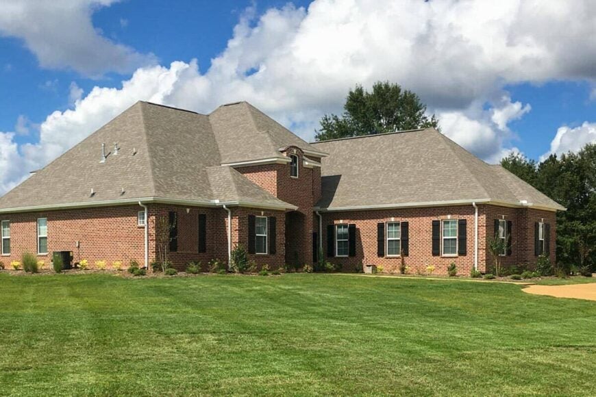 Angled front view showcasing its brick exterior, shuttered windows, and an arched entry.