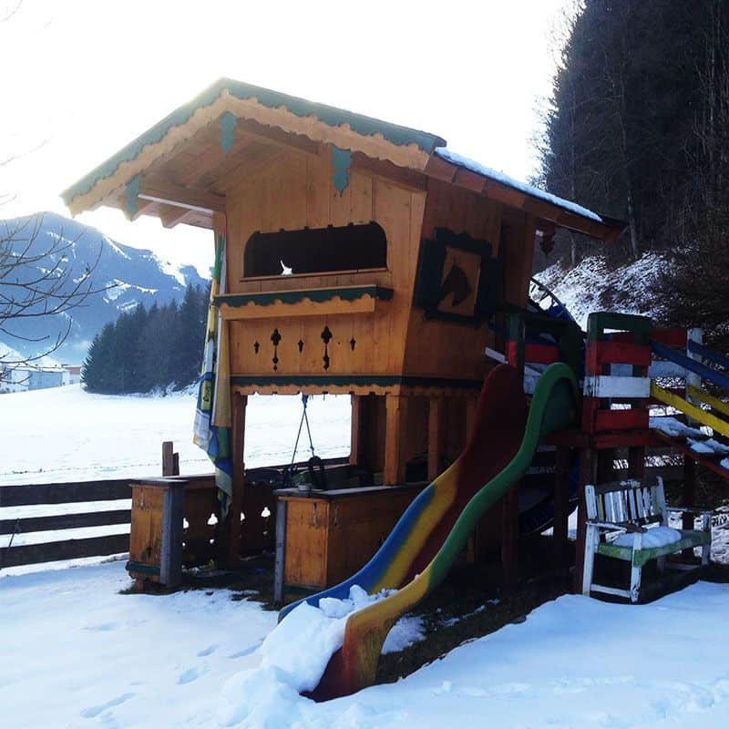 Lookout playhouse with a wooden exterior. It is integrated with a colorful slide on the side.