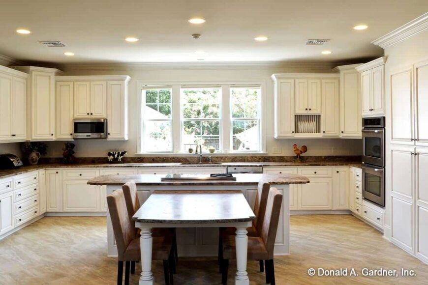 Kitchen with white cabinetry, a center island, and a trio of windows inviting natural light in.