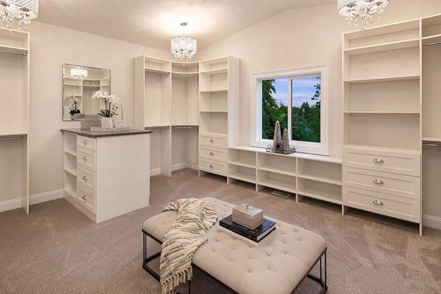 The primary walk-in closet is spacious and filled with ample storage. A counter and a tufted ottoman add nice touches.