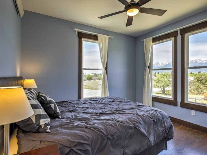 Bedroom with light blue walls and large windows framing a beautiful landscape.