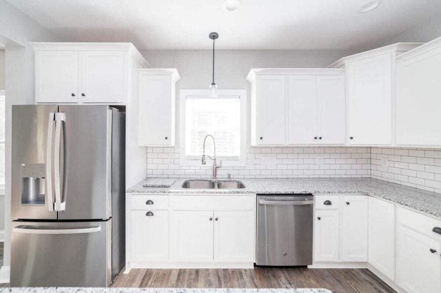 The kitchen includes a white subway tile backsplash and double sinks topped with a small window.