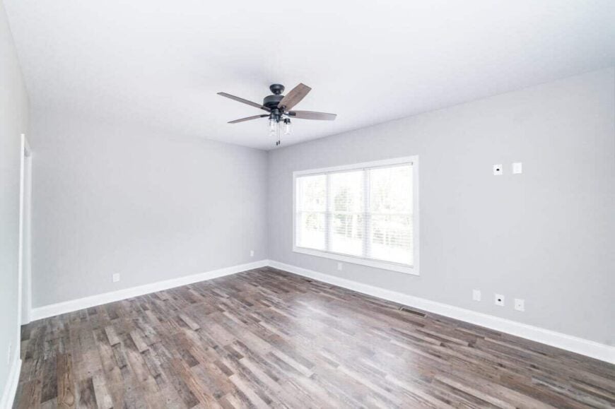 Primary bedroom with a ceiling fan and a trio of windows overlooking the front yard.