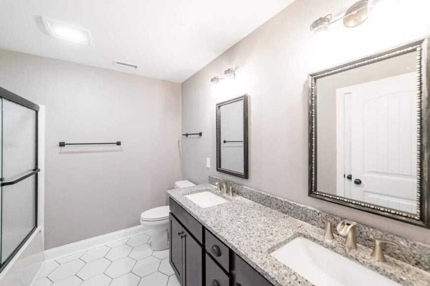 This bathroom is equipped with another dual sink vanity and a toilet over hex tiled flooring.