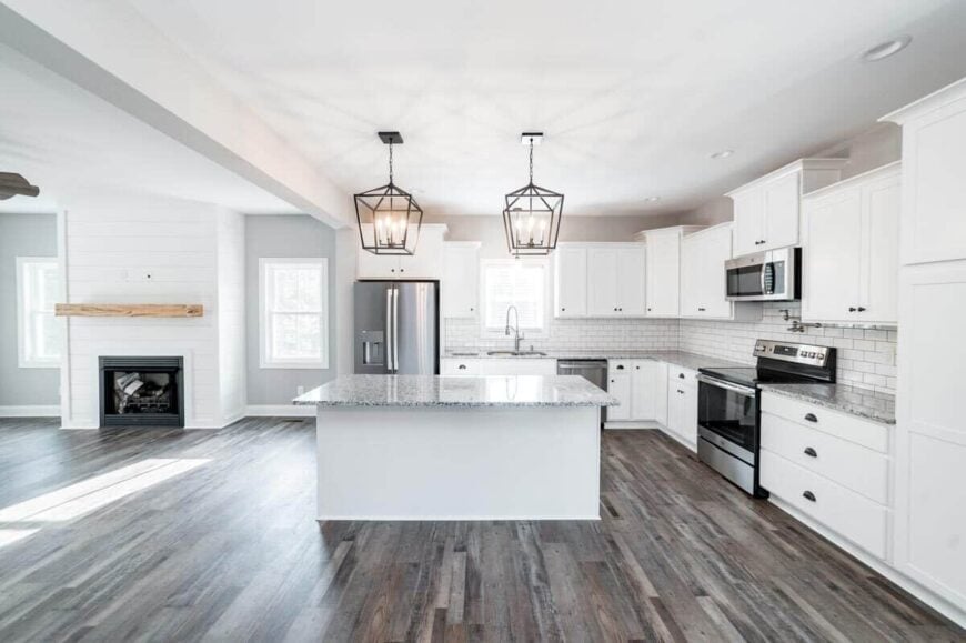 Kitchen with white cabinets, stainless steel appliances, and a center island well-lit by a pair of caged pendants.