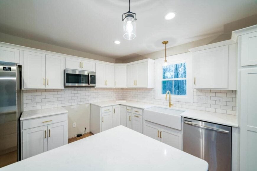The kitchen is equipped with stainless steel appliances, a farmhouse sink, a center island, and white cabinets accentuated with brass hardware.