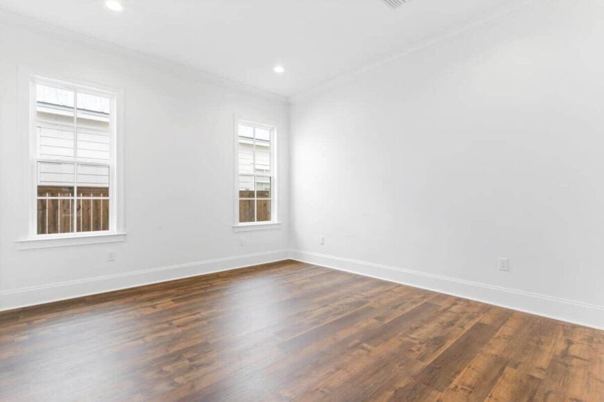Primary bedroom with stark white walls softened by a natural hardwood floor.