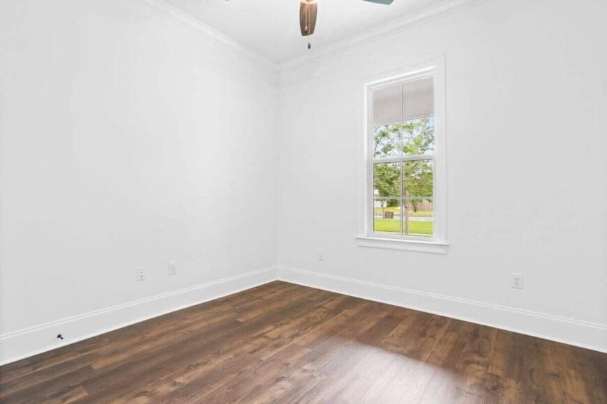 This bedroom has hardwood flooring, white walls, and a framed window allowing natural light in.