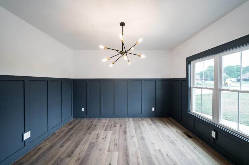 The study has a contemporary chandelier and white walls contrasted by deep blue wainscoting.