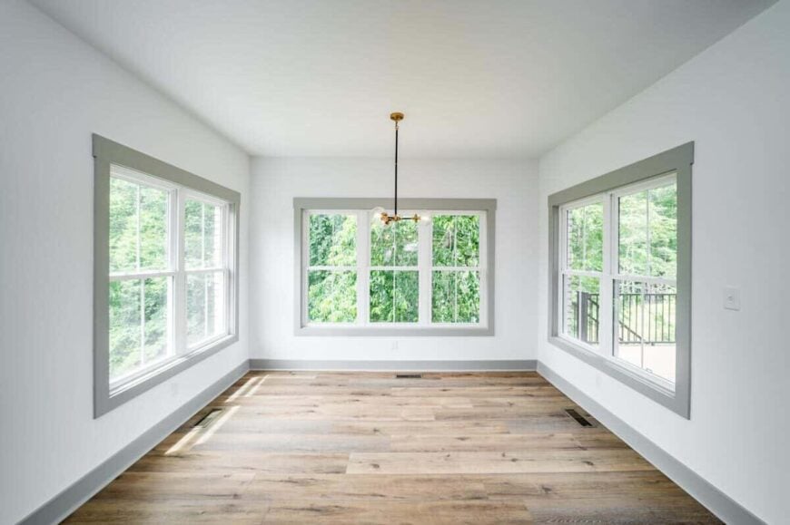 Large windows surround the spacious breakfast nook. It has a sleek pendant light and a natural hardwood floor.