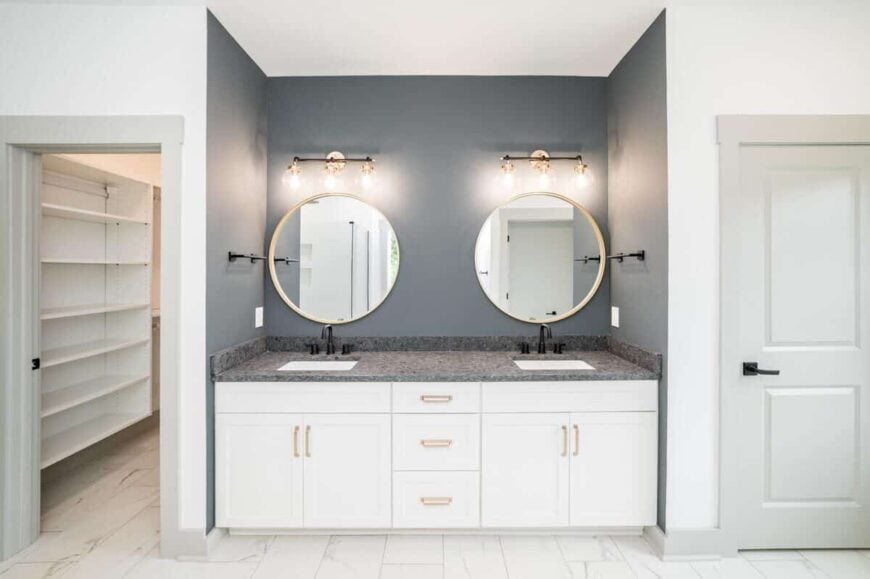 Primary bathroom with a walk-in closet and a dual sink vanity accentuated with brass fixtures and round mirrors.