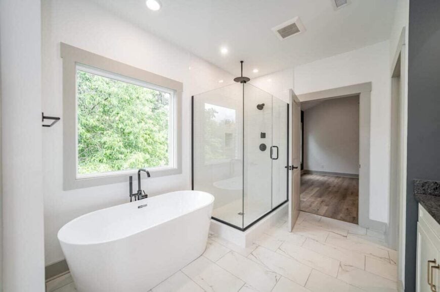 The primary bathroom includes a walk-in shower and a freestanding tub situated beneath the picture window.