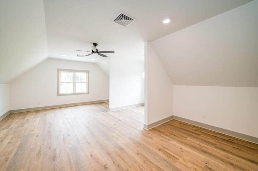Spacious bonus room with hardwood flooring and a vaulted ceiling mounted with a fan.