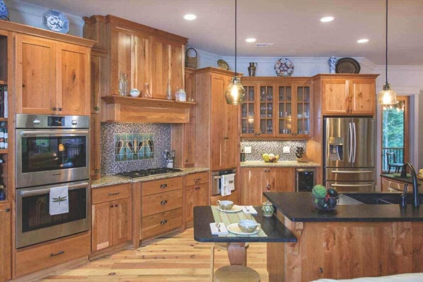 The kitchen is filled with natural wood cabinetry, stainless steel appliances, and a granite-top island set on a wooden base.