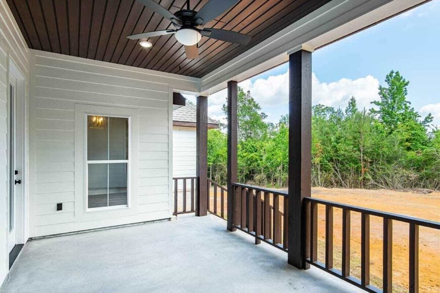 The covered porch has a concrete floor and a wood plank ceiling mounted with a wrought iron fan.