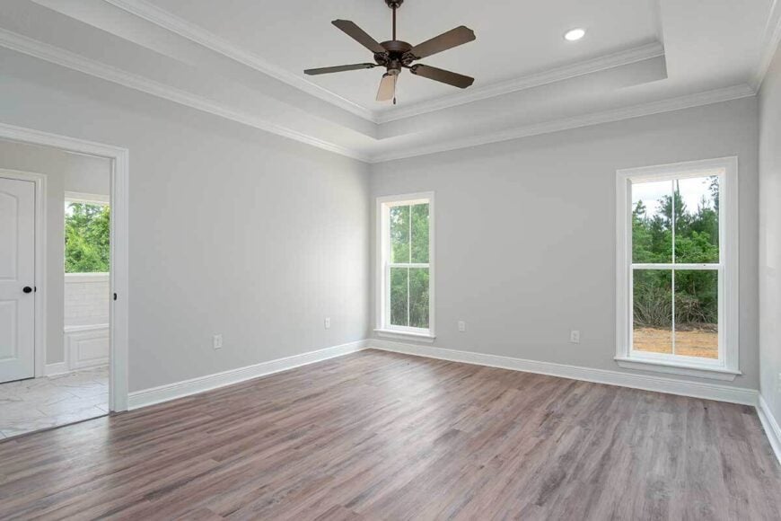 Primary bedroom with hardwood flooring, a tray ceiling, and a private bathroom.