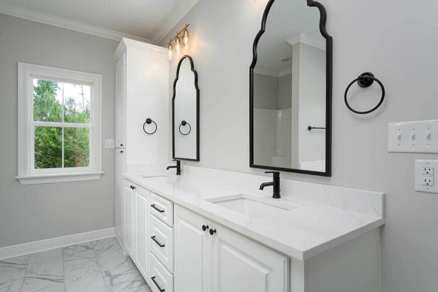 The bathroom vanity is equipped with double sinks, white cabinets, and a pair of arched mirrors.