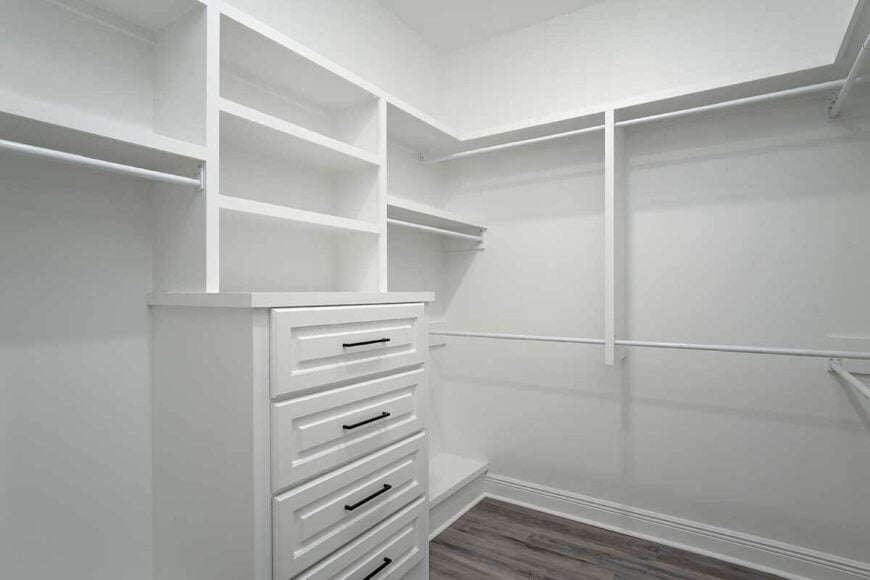 Primary walk-in closet with white drawers and built-in shelves that blend in with the white walls.