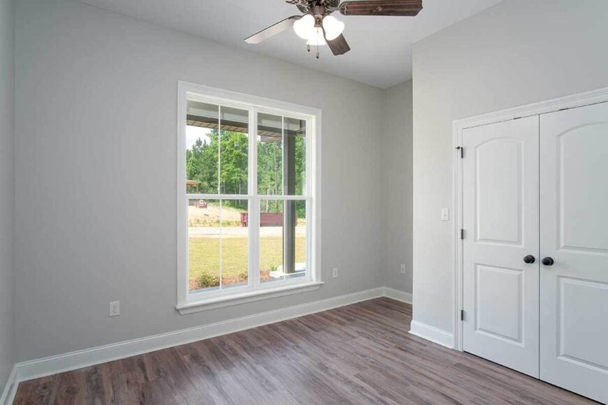 This bedroom has light gray walls and a walk-in closet enclosed with double doors.
