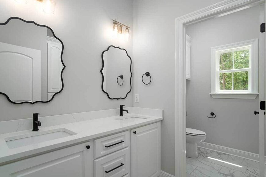 Bathroom with a toilet room and a dual sink vanity topped with decorative mirrors and glass sconces.