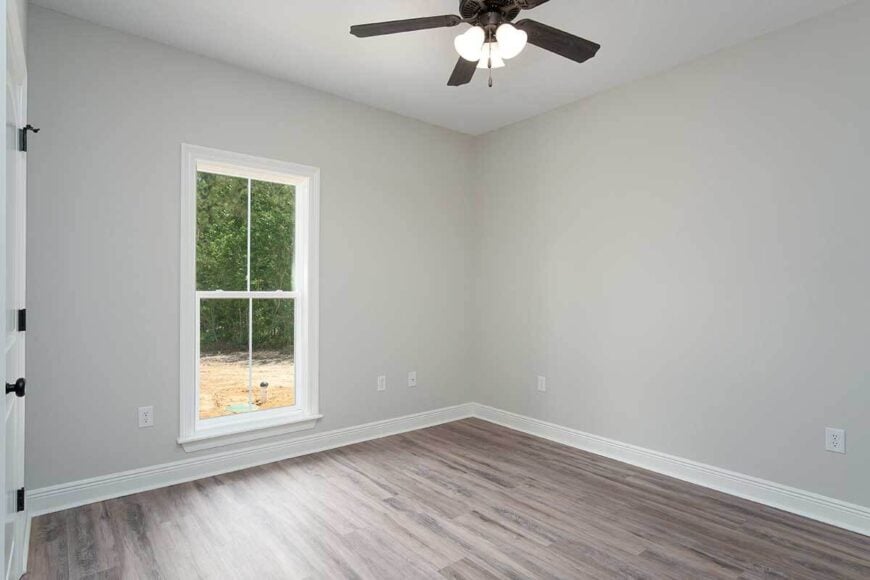 Another bedroom with light gray walls, a hardwood floor, and a white framed window.