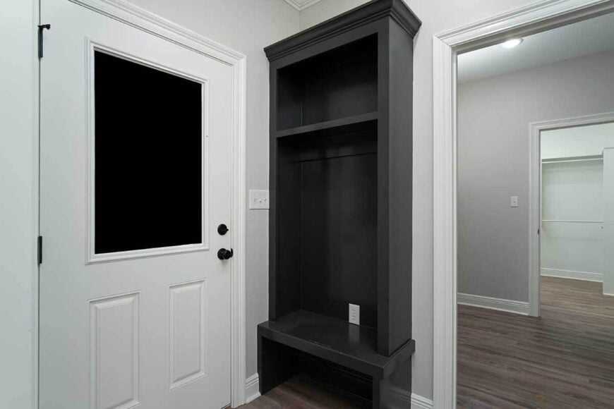 A black built-in bench with a shelf and coat rack stands out against the light gray walls of the mudroom.