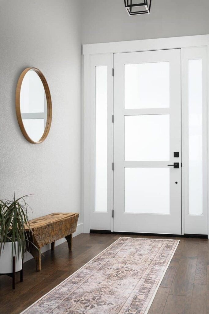 Foyer with a glazed entry door, a vintage area rug, and a wicker bench adorned with a round mirror.