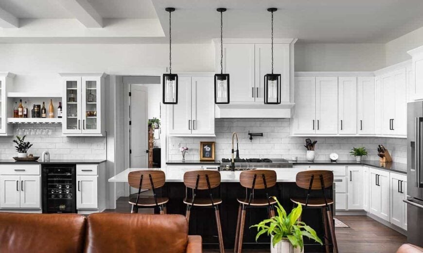 Kitchen with white cabinetry, marble subway tiled backsplash, and a breakfast island lined with wooden bar stools.