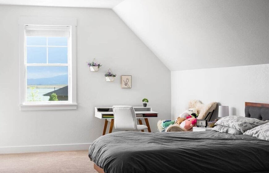 Kid's bedroom with vaulted ceiling, a carpeted floor, and a tufted bed complemented with a furry chair and a wooden desk.