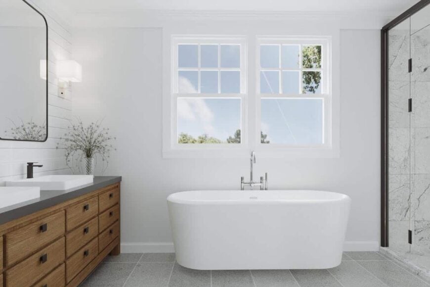 Primary bathroom with dual sink vanity and a freestanding tub placed under the white framed windows.
