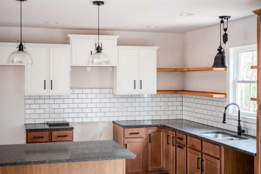 The kitchen includes contrasting white and wooden cabinets, double sinks, and floating shelves mounted above the white subway tile backsplash.