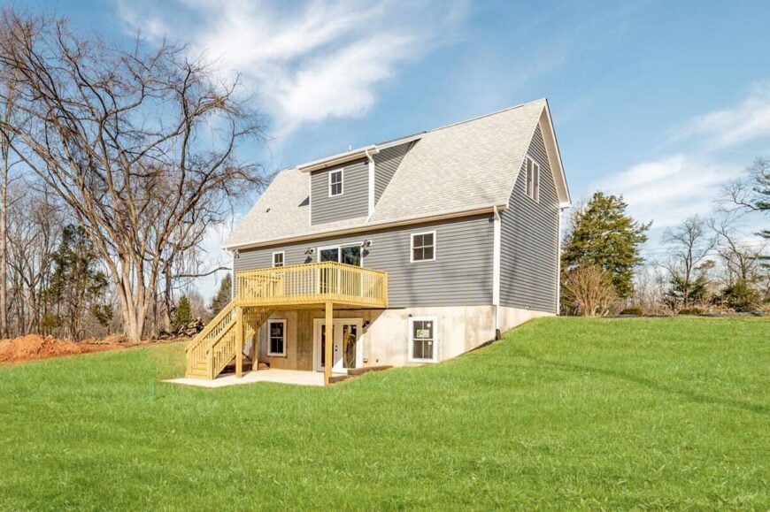 Rear exterior view showcasing a walkout basement and a grilling deck supported by wooden columns.