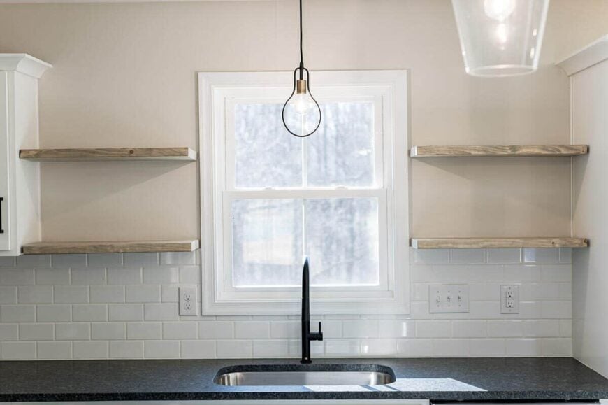 Floating shelves mounted above the subway tile backsplash flank the white framed window.