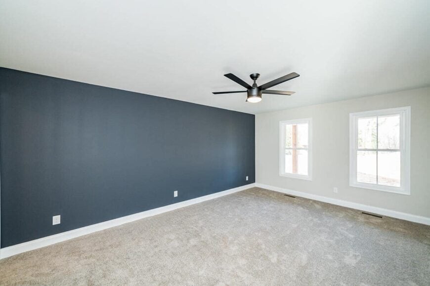 Primary bedroom with carpeted floor, a deep blue accent wall, and a wrought ceiling fan.