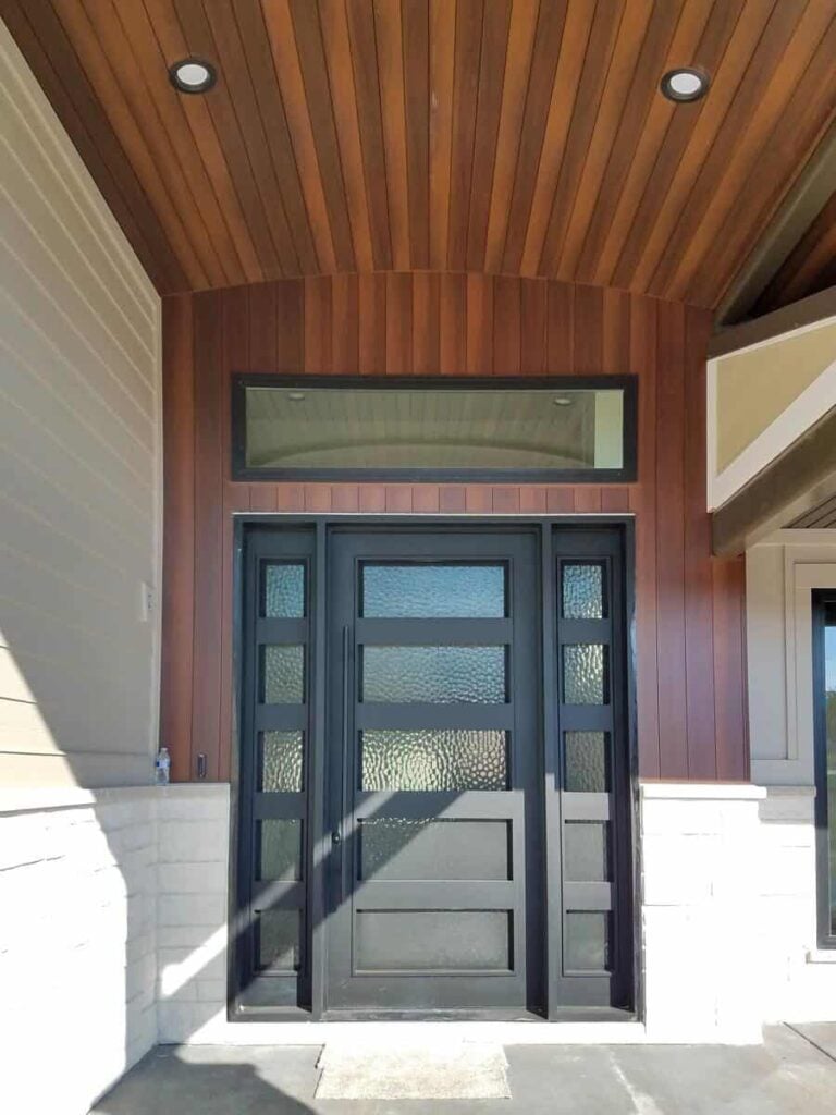The entry porch includes wood paneled accents and a glazed front door framed with side panels and a transom window.