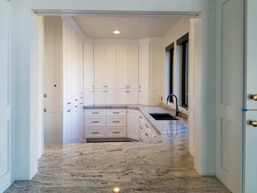 Lower-level kitchenette with tall cabinets, granite countertops, and double sinks fitted with a gooseneck faucet.