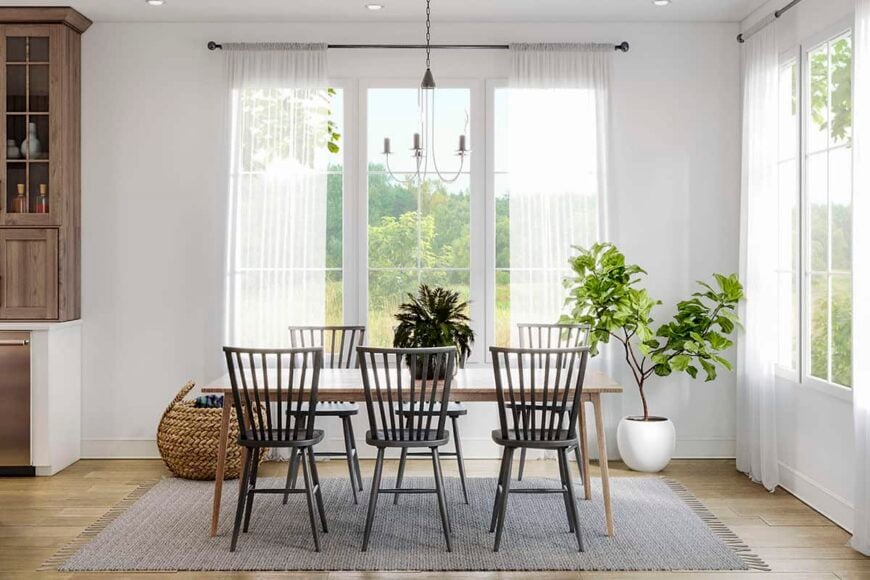 The dining area has a light and airy vibe with a fresh potted plant and large windows dressed in sheer curtains.