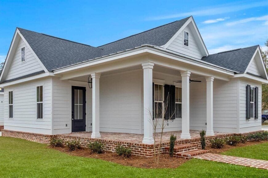 Covered entry porch with brick flooring, a stoop, white columns, and a glazed front door.