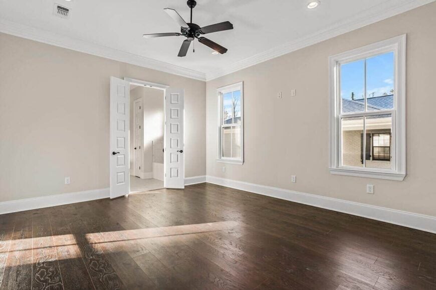 Primary bedroom with wide plank flooring, a private bathroom, and white framed windows that bring natural light in.