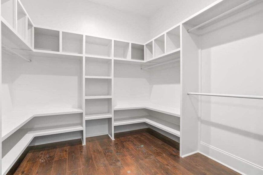 Primary walk-in closet with built-in shelves that blend in with the white walls.