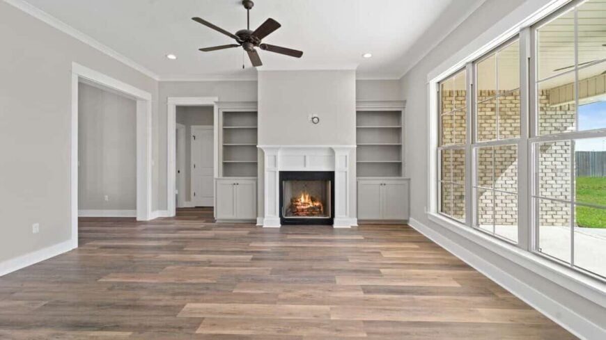 Great room with large windows and a fireplace flanked by built-in shelves and base cabinets.