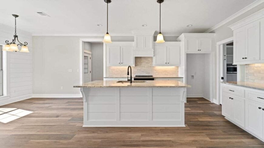 The kitchen offers white cabinetry, granite countertops, and a breakfast island topped with warm pendant lights.