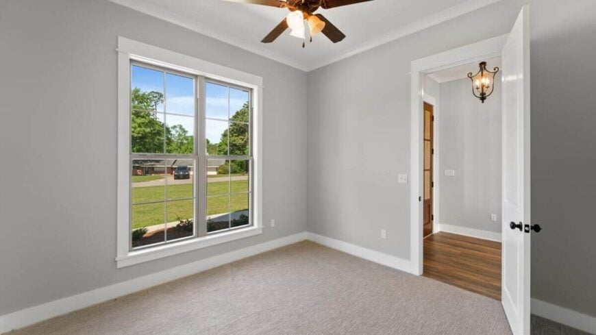 Another bedroom with carpet flooring, a framed window, and a ceiling fan with warm lamps.