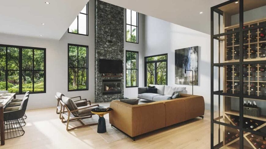 The living room has a tall ceiling, a stone fireplace, and a gallery of windows bringing an abundant amount of natural light in.