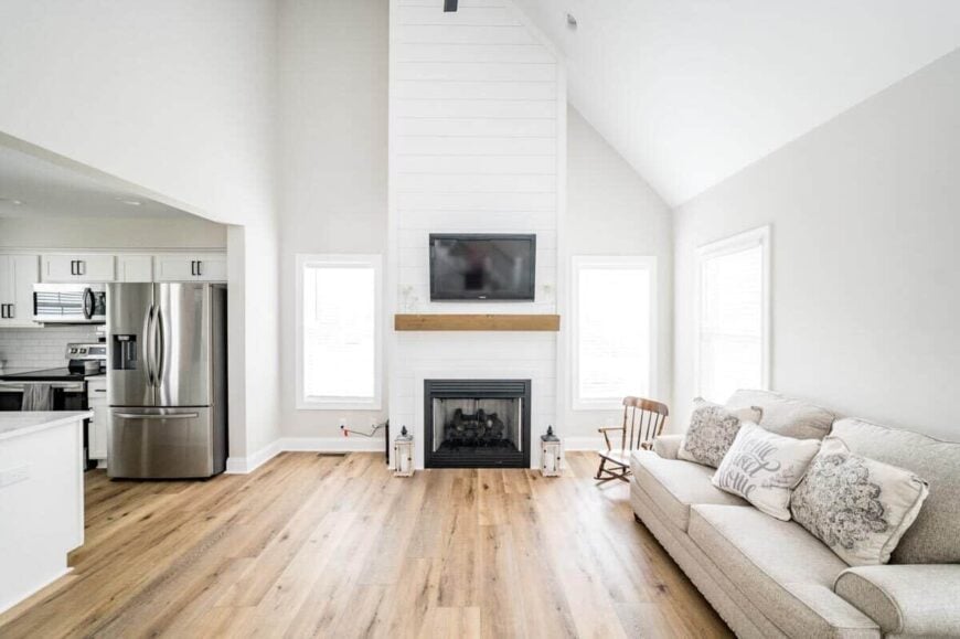 The great room has a high vaulted ceiling, a gray sectional, and a fireplace topped with a TV.